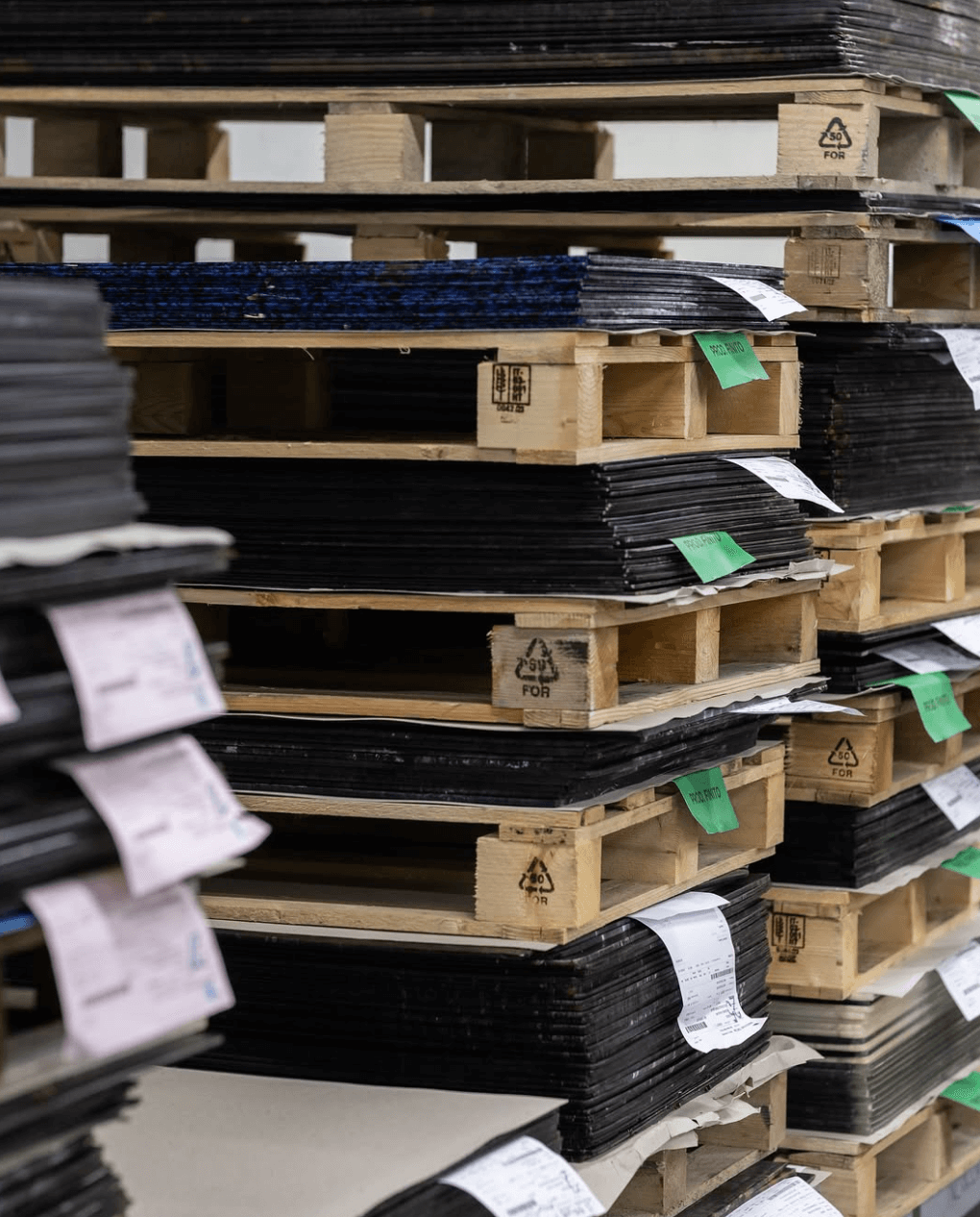 Stacks of wooden pallets with plastic materials on top in a warehouse setting